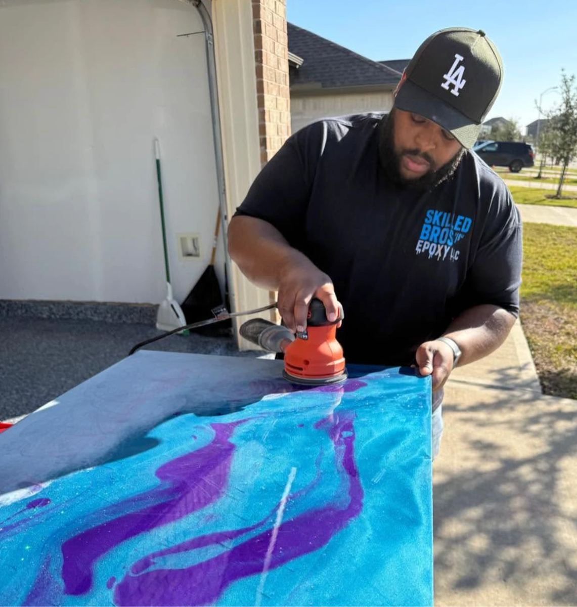 Denzel Washington sanding a blue and purple metallic epoxy countertop in his Skilled Bros shirt